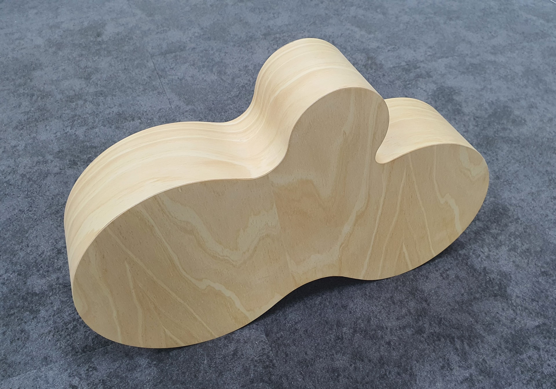 CNC-cut plywood cloud-shaped display/fixture with layered edges, photographed on a grey carpeted floor — finished wooden prototype or retail/event prop.