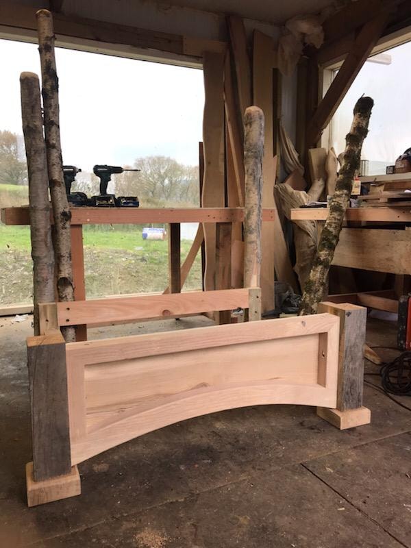 Handcrafted solid wood panel and frame under construction in a workshop, shown with birch uprights and power tools in the background.