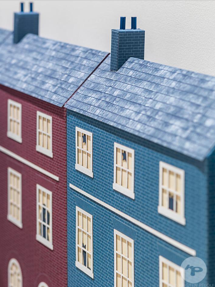 High-detail architectural scale model of terraced houses with precise window cut-outs and textured roofs, photographed with shallow depth of field for a design presentation.