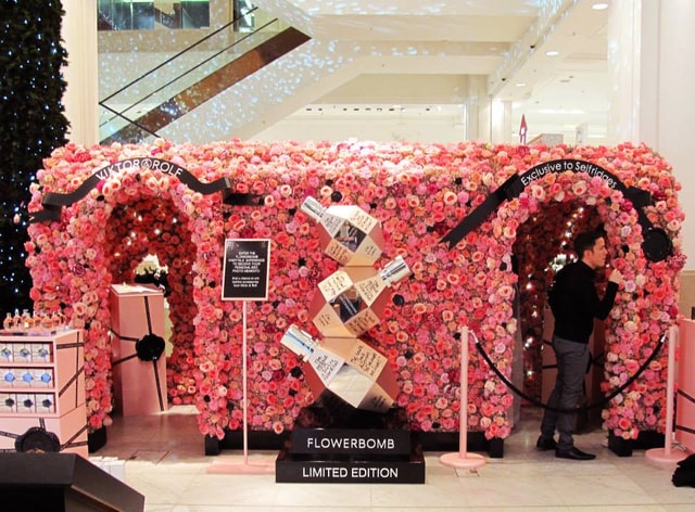 Temporary Flowerbomb promotional installation covered in pink flowers with large perfume bottle sculpture and visible Viktor&Rolf / Selfridges branding inside a department store.