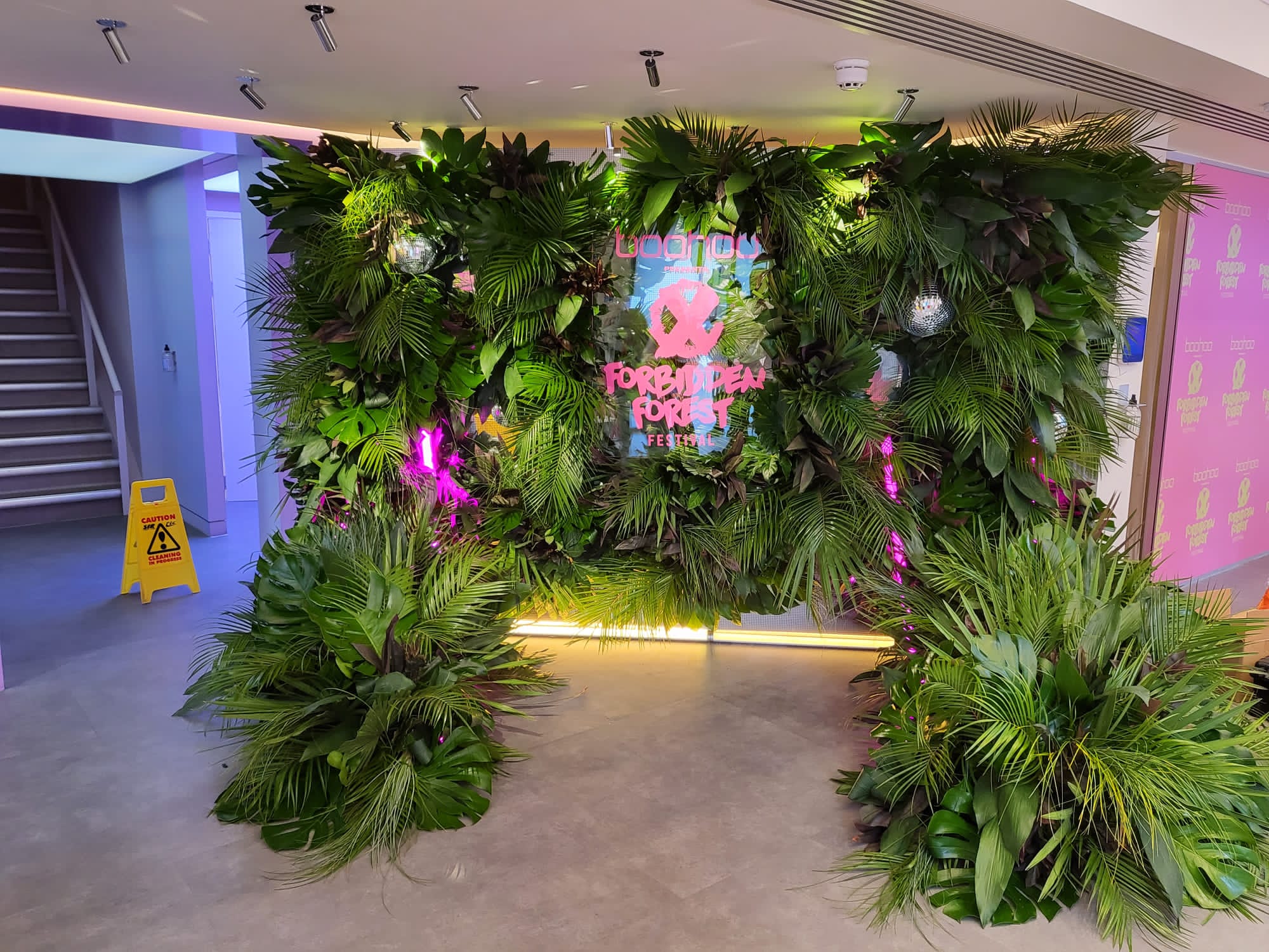 Indoor living wall event backdrop with neon branded sign, disco balls and accent lighting used for a festival activation in a lobby space.