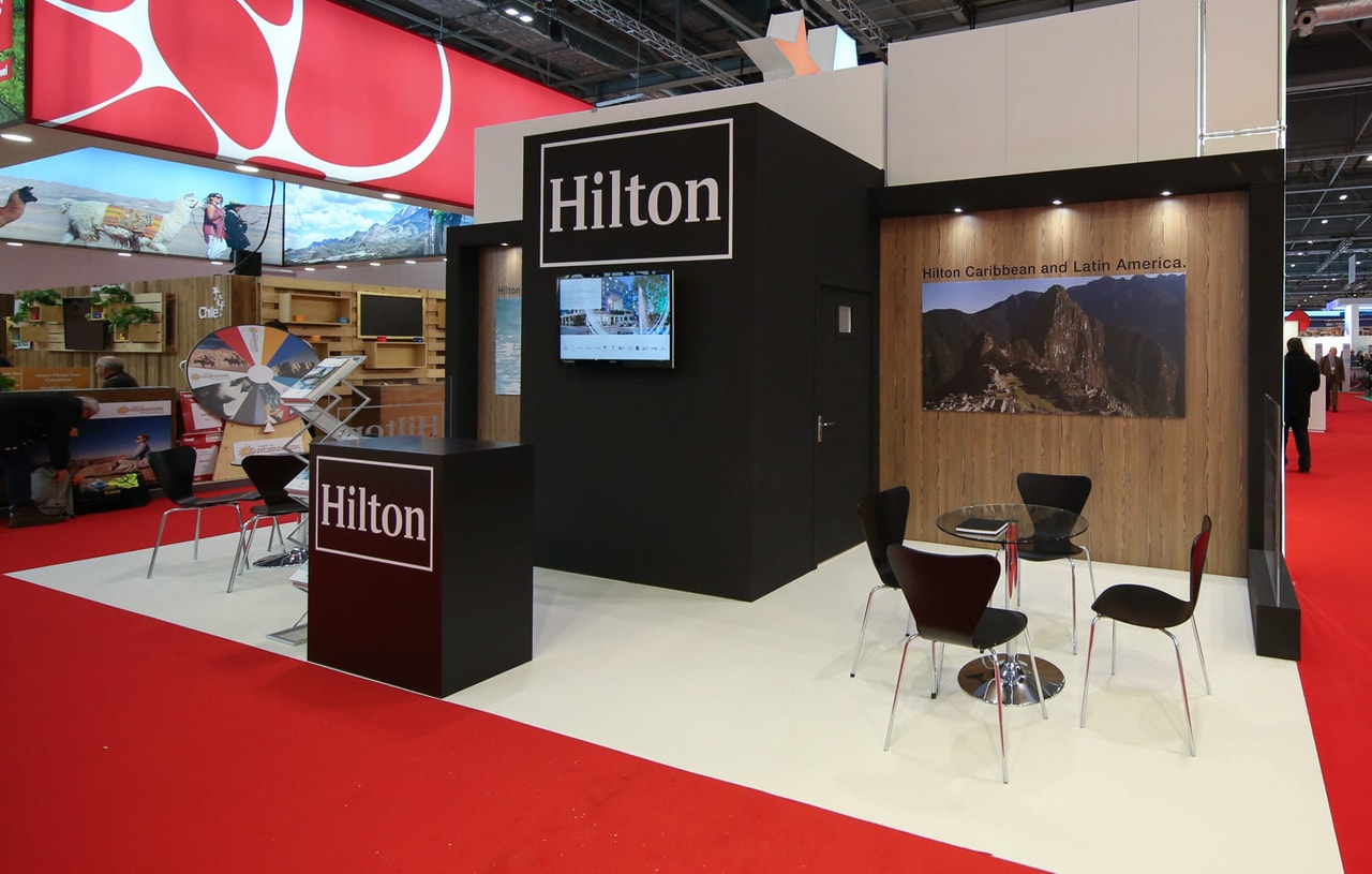 Hilton exhibition stand at a trade show with branded signage, a reception counter and a small meeting area, showcasing a finished event booth installation.
