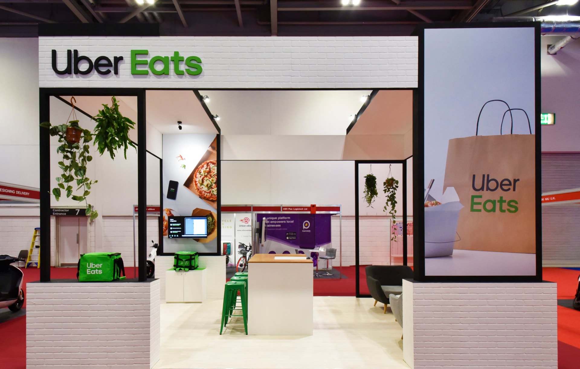 Uber Eats branded exhibition stand at a trade show featuring large printed panels, digital displays and demo counters in an open-plan booth.