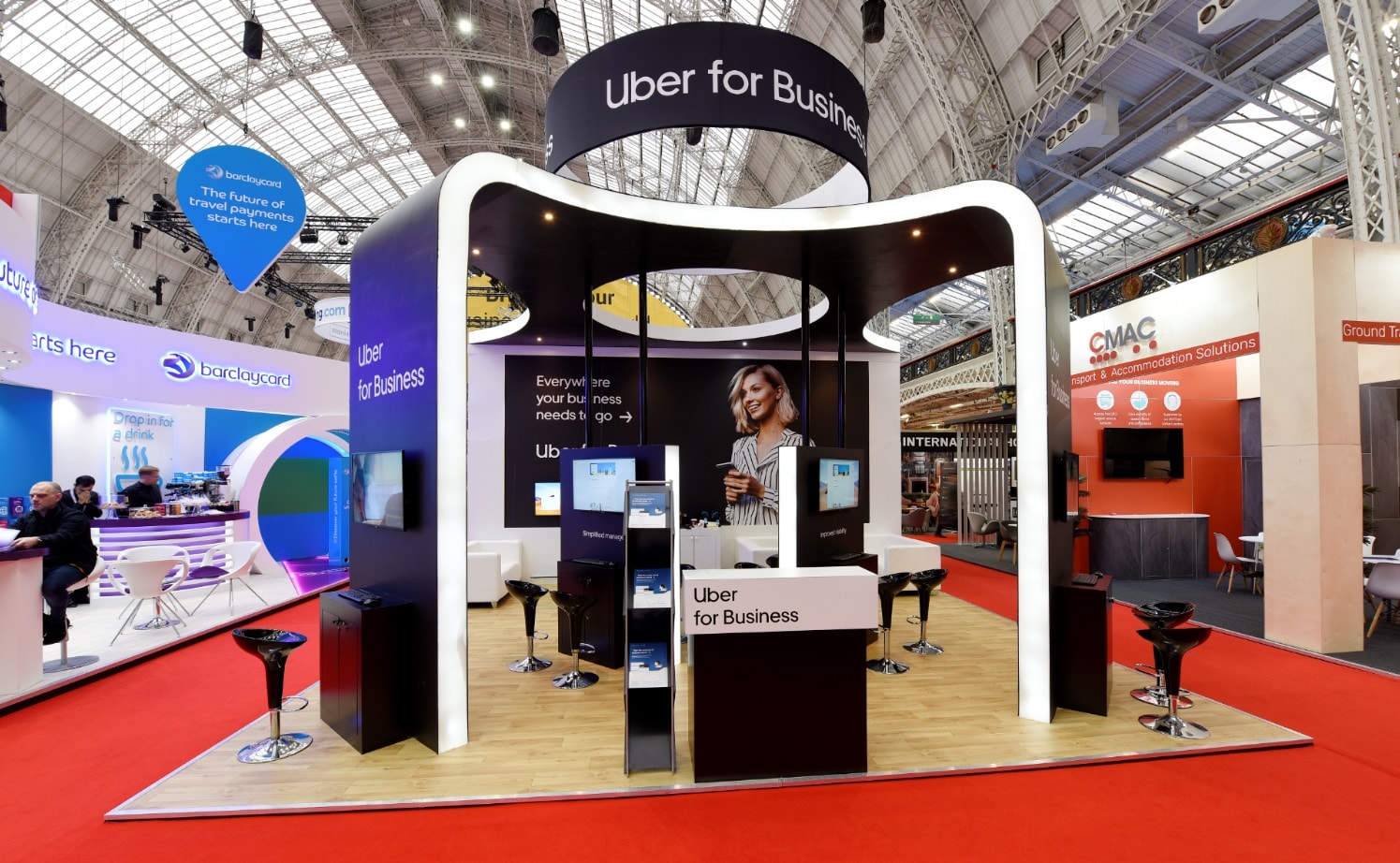 Uber for Business exhibition stand with curved illuminated canopy, branded backwall graphics, hanging banner and demo kiosks at a trade show.