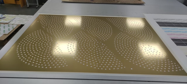 Perforated gold panel with a patterned array of circular holes laid out on a workshop table, likely produced by laser cutting for decorative or architectural use.