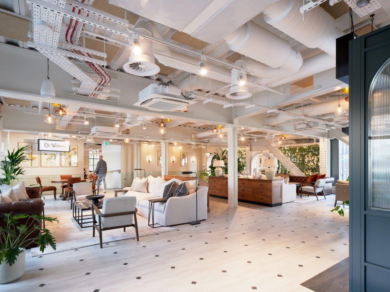 Bright, finished coworking lounge with sofas, feature lighting and exposed ceiling services, showcasing a contemporary office interior fit-out.