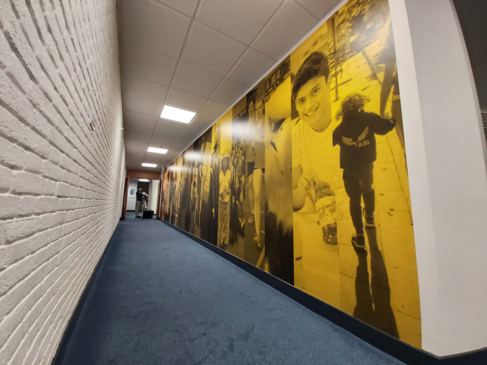 Large-format printed wall mural installed as a feature wall in a modern office corridor with yellow accents.