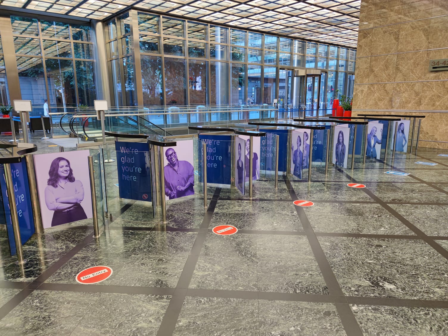 Installed large-format printed welcome panels on turnstiles in a glass office lobby, with floor social-distancing decals and stainless steel fixtures.