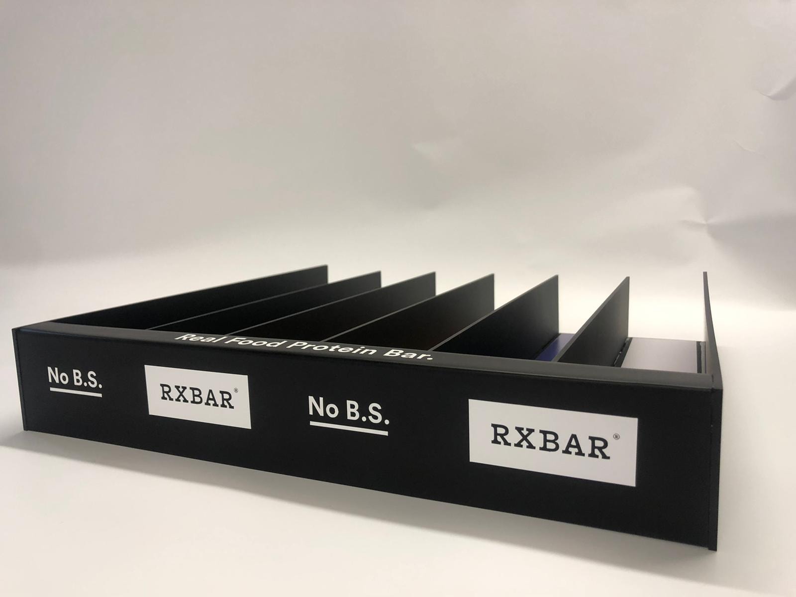 Clear acrylic RXBAR product display stand photographed in studio setting.