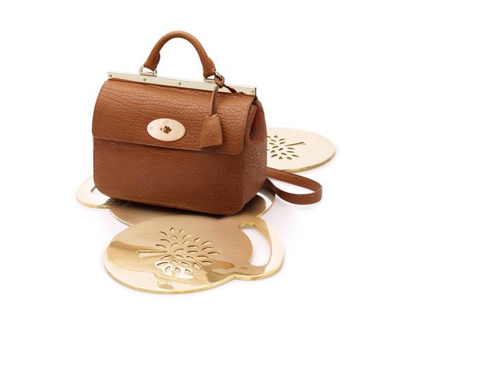 Gold acrylic display stand for leather handbag in studio setting.