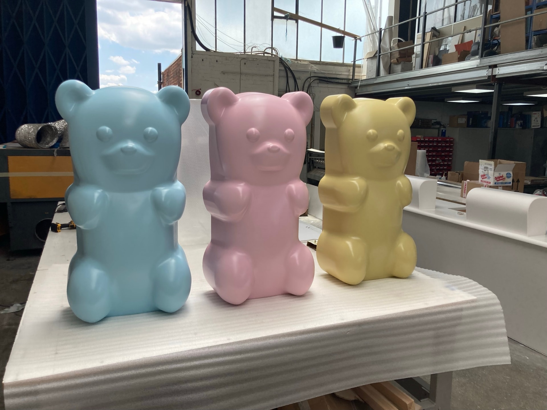 Three pastel vacuum-formed bear-shaped display fixtures on a workshop bench, likely finished retail props or point-of-sale displays produced in a fabrication shop.