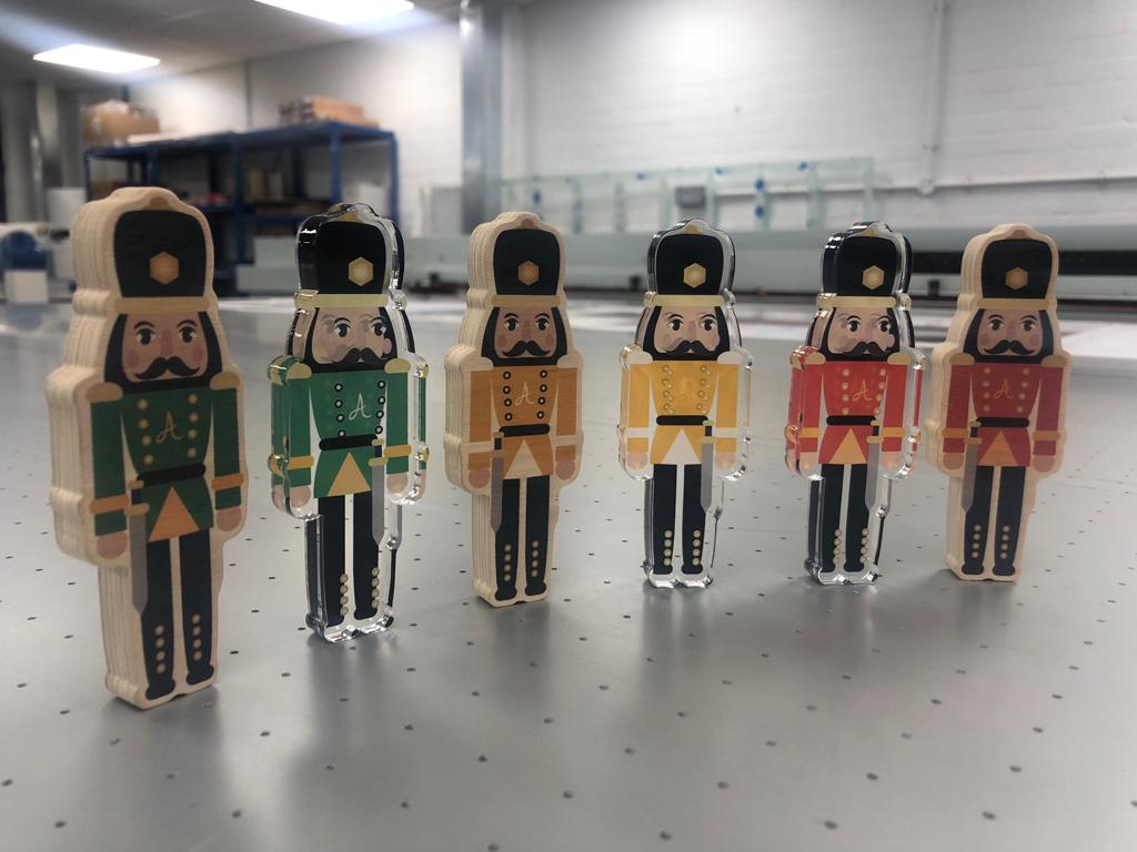 Finished plywood and acrylic nutcracker figure cutouts with printed graphics on a production table in a workshop, suitable as small POS/display items.