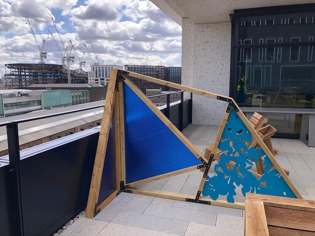 Finished triangular wooden and blue plastic decorative screen installed on a rooftop terrace, featuring a corrugated panel and a laser-cut decorative panel.
