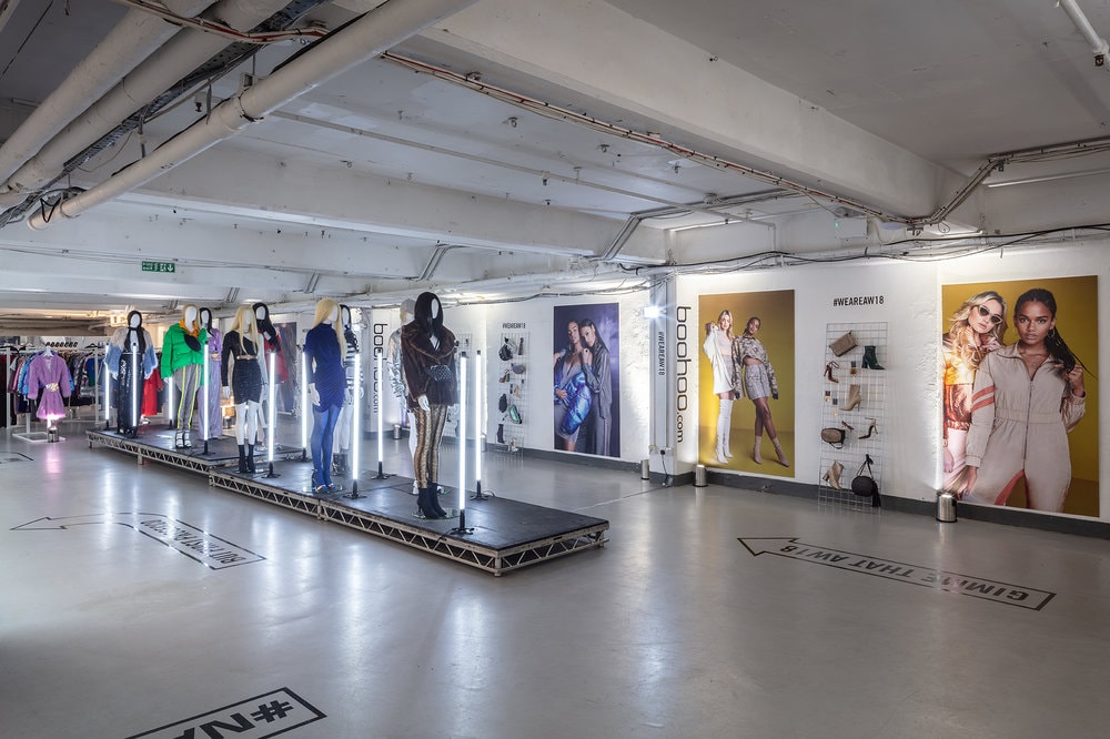 Interior pop-up retail space with a runway of mannequins, illuminated vertical lights and large-format branded wall graphics for a Boohoo campaign.