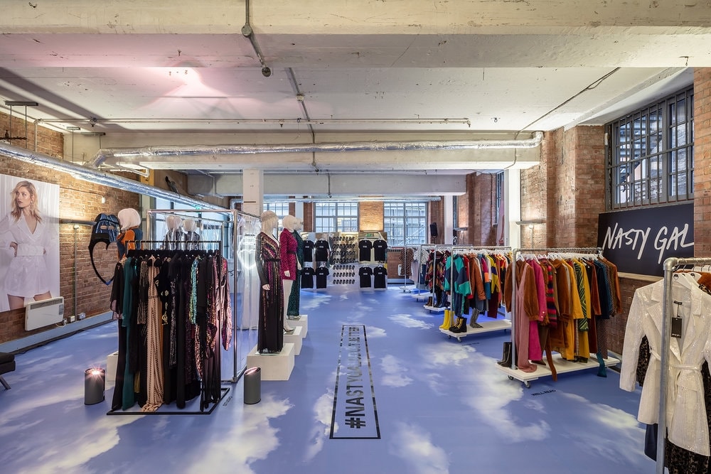 Interior of a Nasty Gal pop-up retail space in an industrial loft, featuring clothing racks, mannequins and prominent branded wall signage.