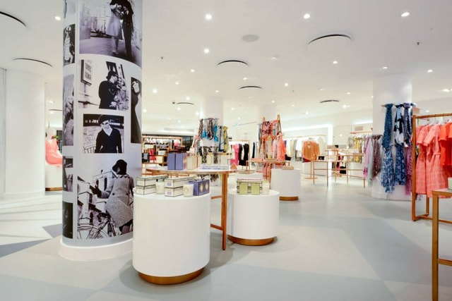 Bright, modern retail store interior with circular product displays, clothing racks and a graphic-wrapped pillar, showcasing merchandising and in-store fixtures.