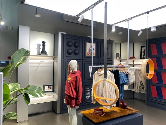 Interior shot of a New Balance retail store showing a mannequin, clothing racks and bespoke display fixtures in a well-lit store environment.
