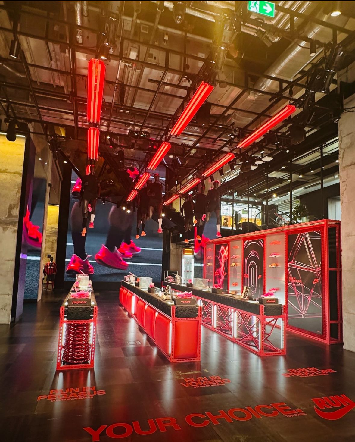High-impact Nike retail installation with illuminated red display counters, large video wall and branded floor graphics showcasing footwear.