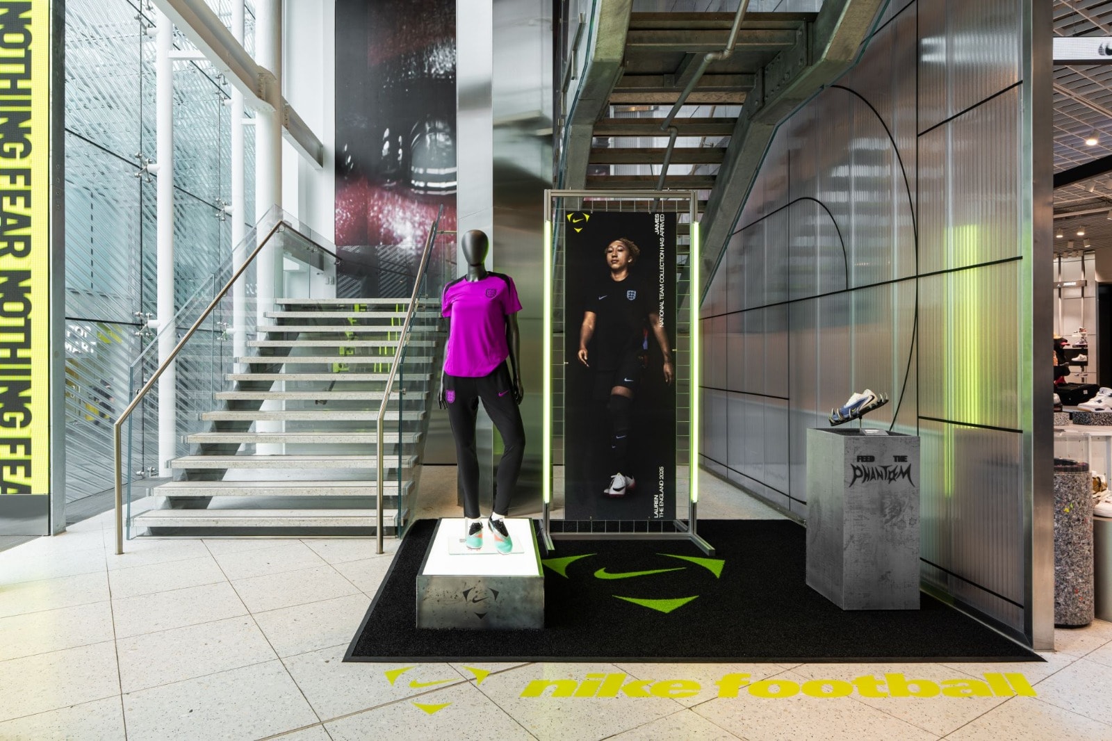 Nike in-store retail display featuring a mannequin on an illuminated plinth, a large-format printed athlete banner, concrete shoe plinth and branded floor graphics, set within a modern store interior.