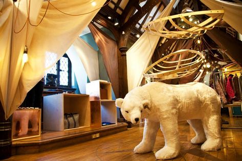 Stylish boutique retail interior with wooden display fixtures, hanging fabric elements and a large plush polar bear prop creating an immersive merchandising installation.