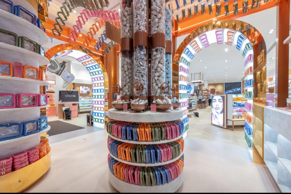 Bright Space NK retail interior featuring a central circular display with colorful product pouches, arched shelving and visible brand signage — ideal example of retail merchandising and fixtures.