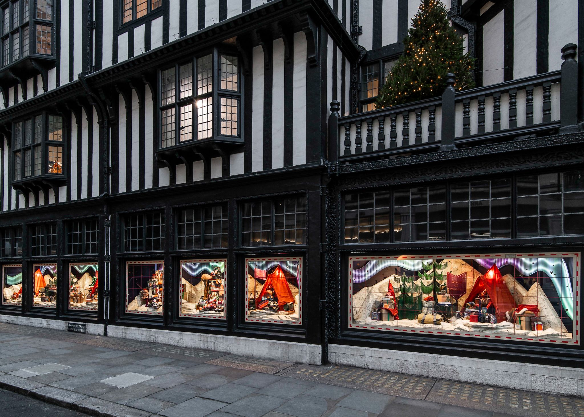 Exterior view of a historic retail storefront with multiple illuminated seasonal window displays and street-facing merchandising.