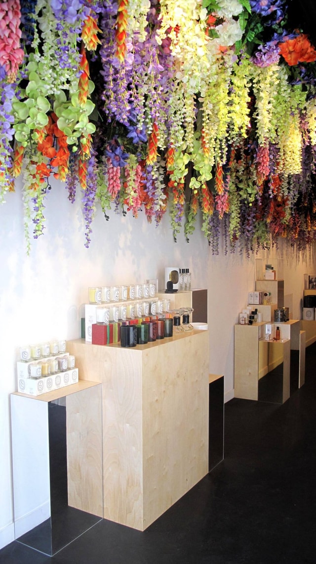 Bright retail interior with wooden display plinths showcasing products beneath a dramatic hanging floral ceiling installation, ideal for boutique shop visuals.