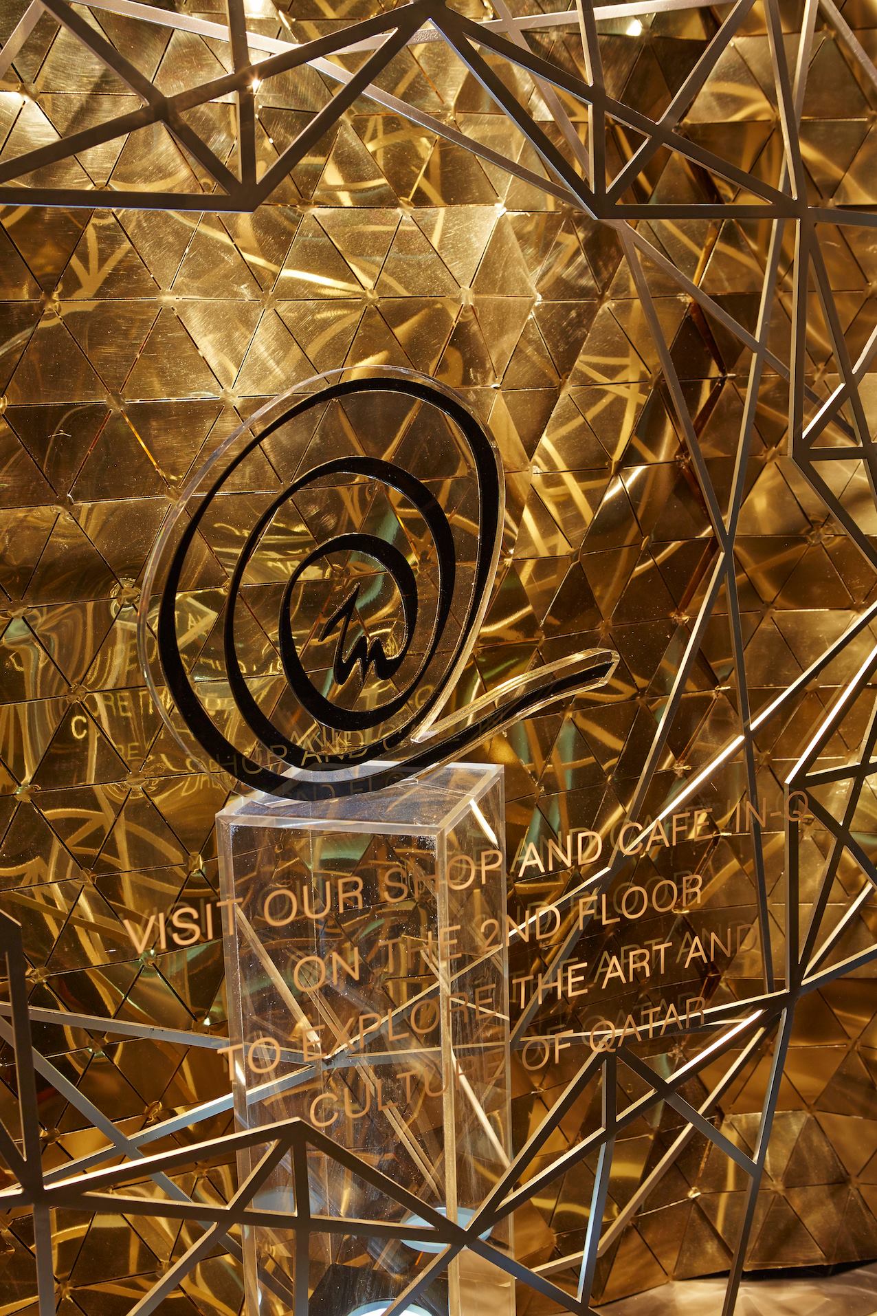 Gold tessellated retail window display with a black spiral logo on glass, acrylic plinth and gold lettering promoting the shop and cafe.
