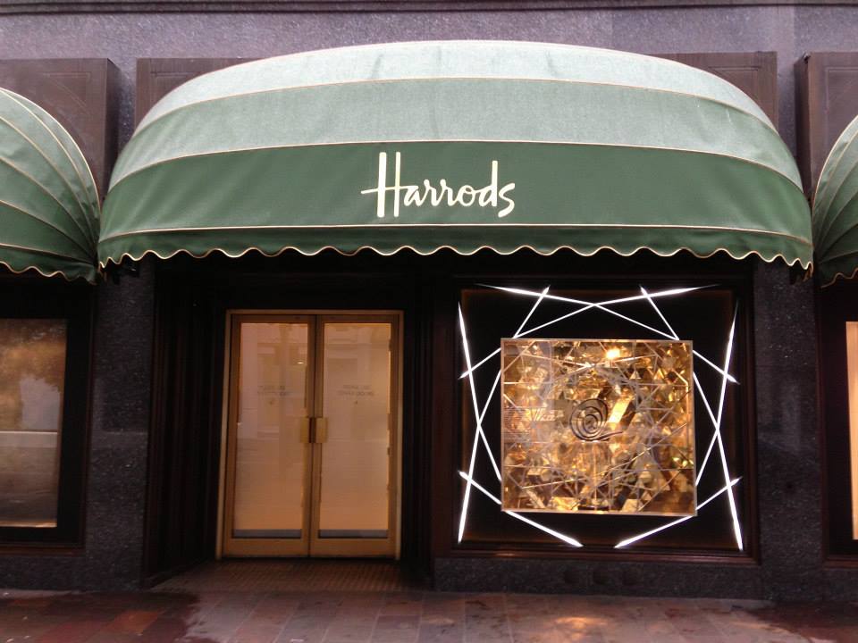 Harrods storefront with branded green awning and illuminated window display framed by geometric LED lighting, showcasing premium retail signage and window manifestation.