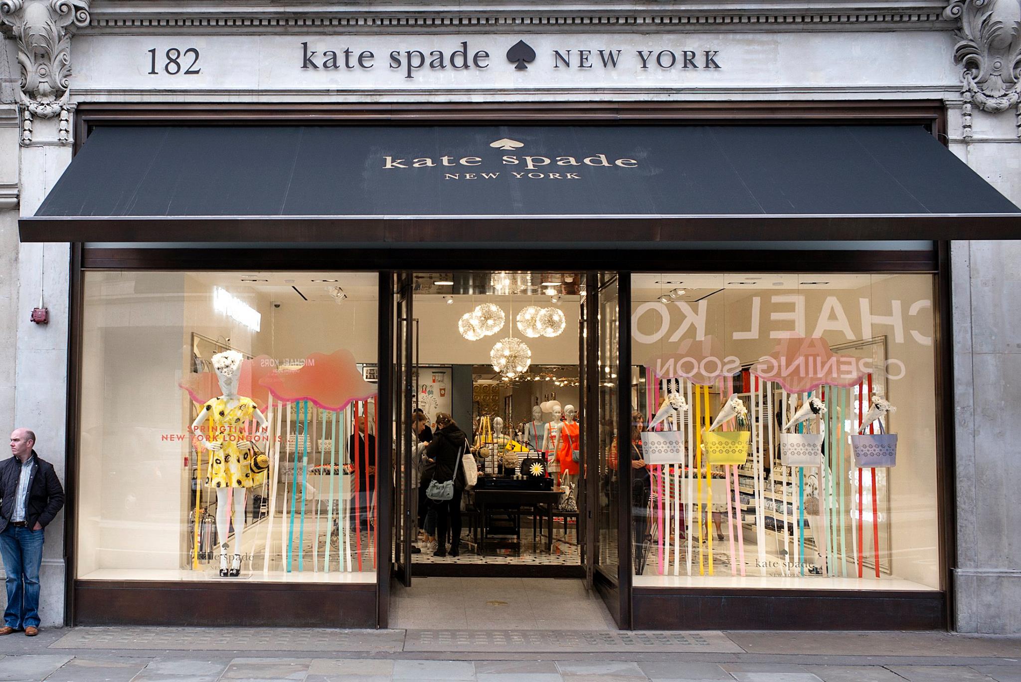 Kate Spade New York storefront with branded fascia and awning, large window displays featuring mannequins and colourful vinyl window graphics.