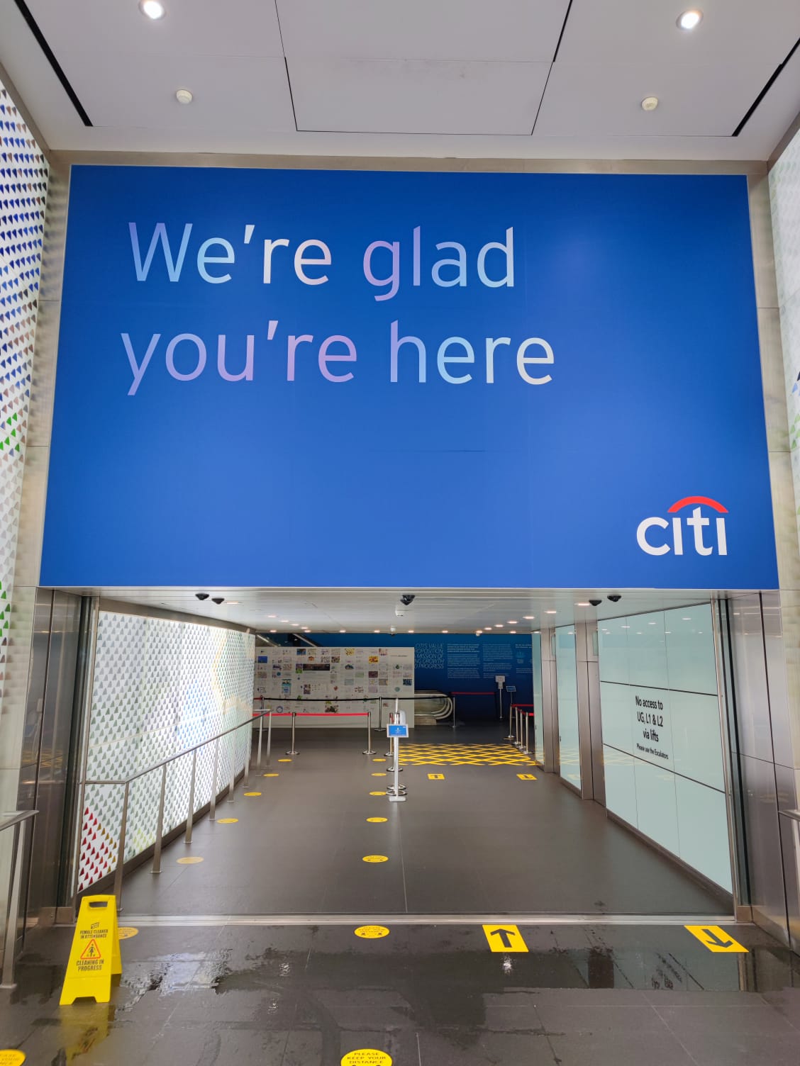 Installed large-format branded wall graphic in a bank lobby reading 'We're glad you're here' with the Citi logo, photographed from the entrance.
