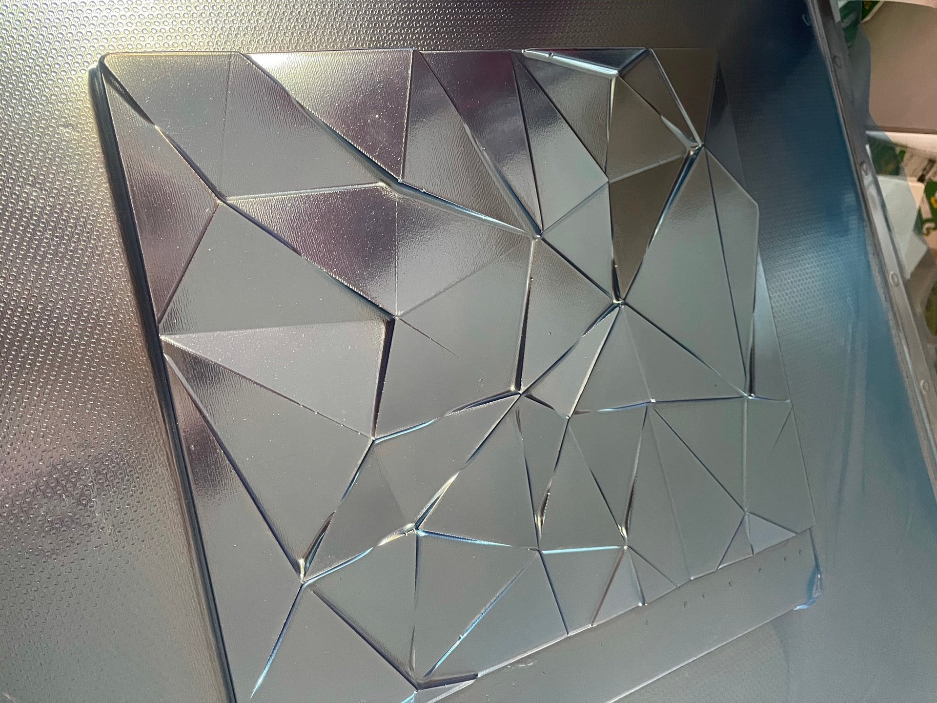 Vacuum-formed faceted plastic panel on a textured vacuum bed, showing the formed geometry and finished glossy surface.