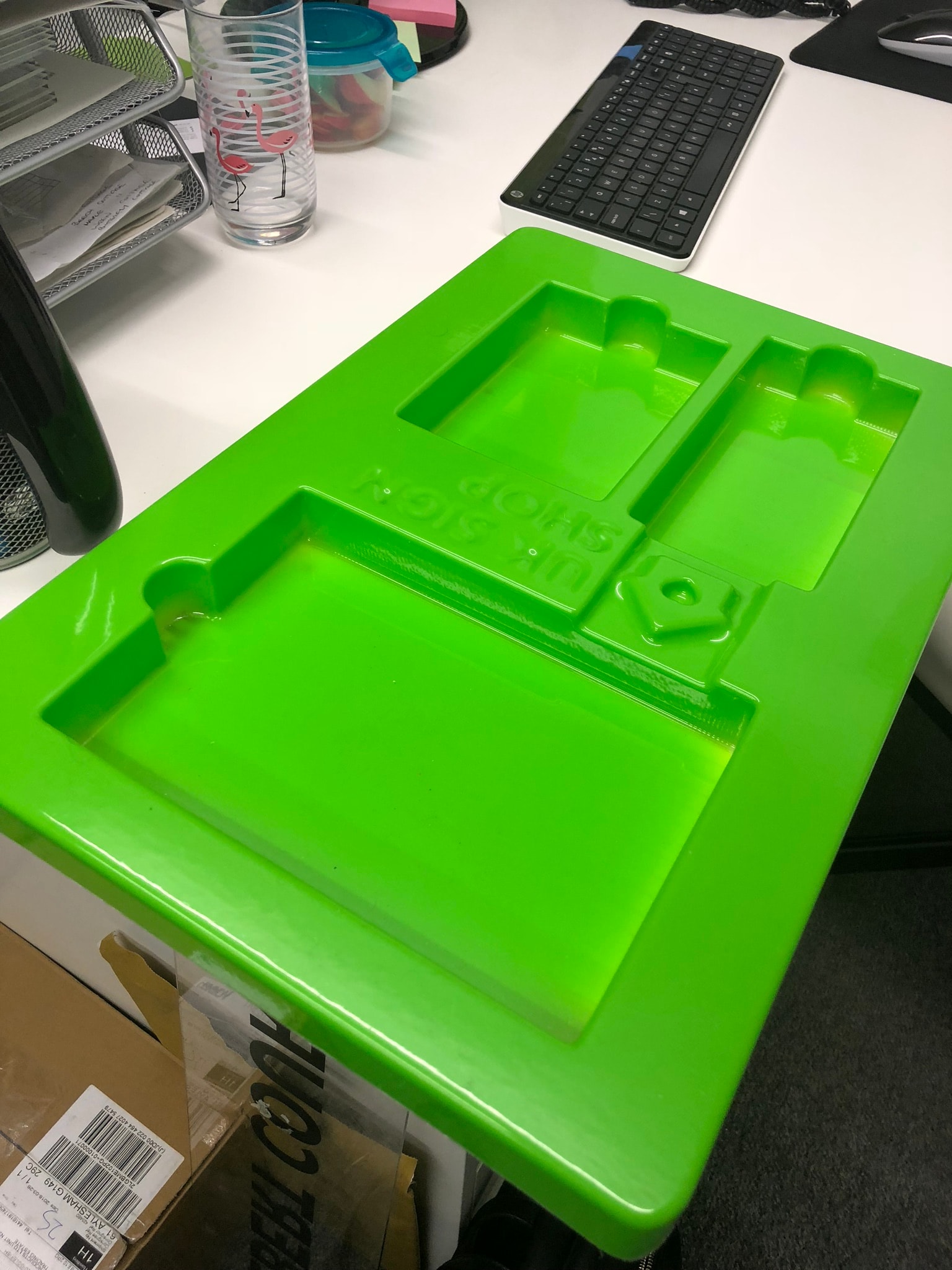 Bright green vacuum-formed plastic tray with multiple cavities, shown as a finished packaging/display insert on a desk.