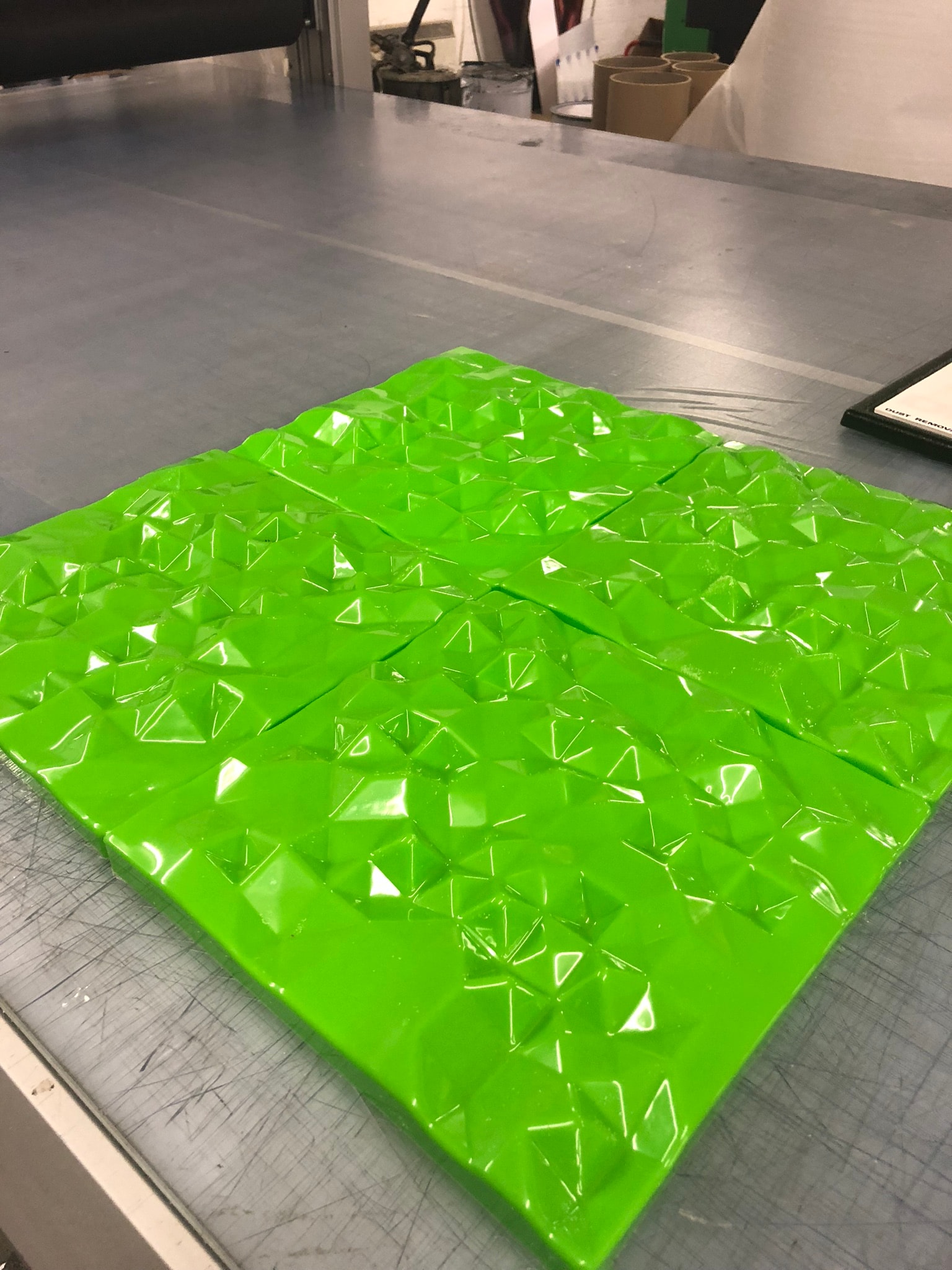 Bright green vacuum-formed plastic panel with a geometric pyramid texture placed on a workshop table, showing a finished thermoformed sheet ready for trimming or assembly.