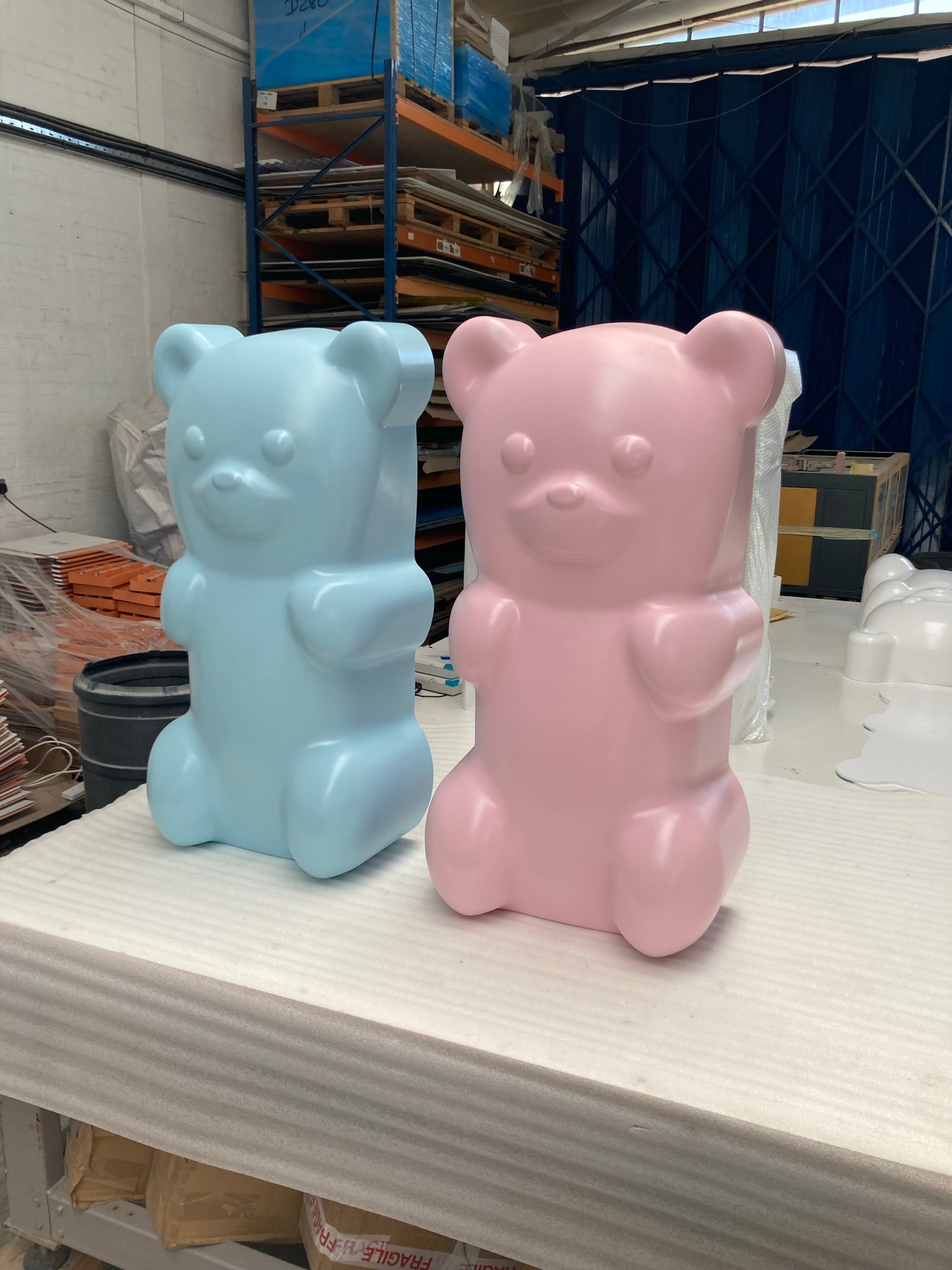 Pastel pink and blue vacuum-formed bear-shaped plastic shells displayed on a workshop bench, likely finished display pieces or props in a fabrication shop.