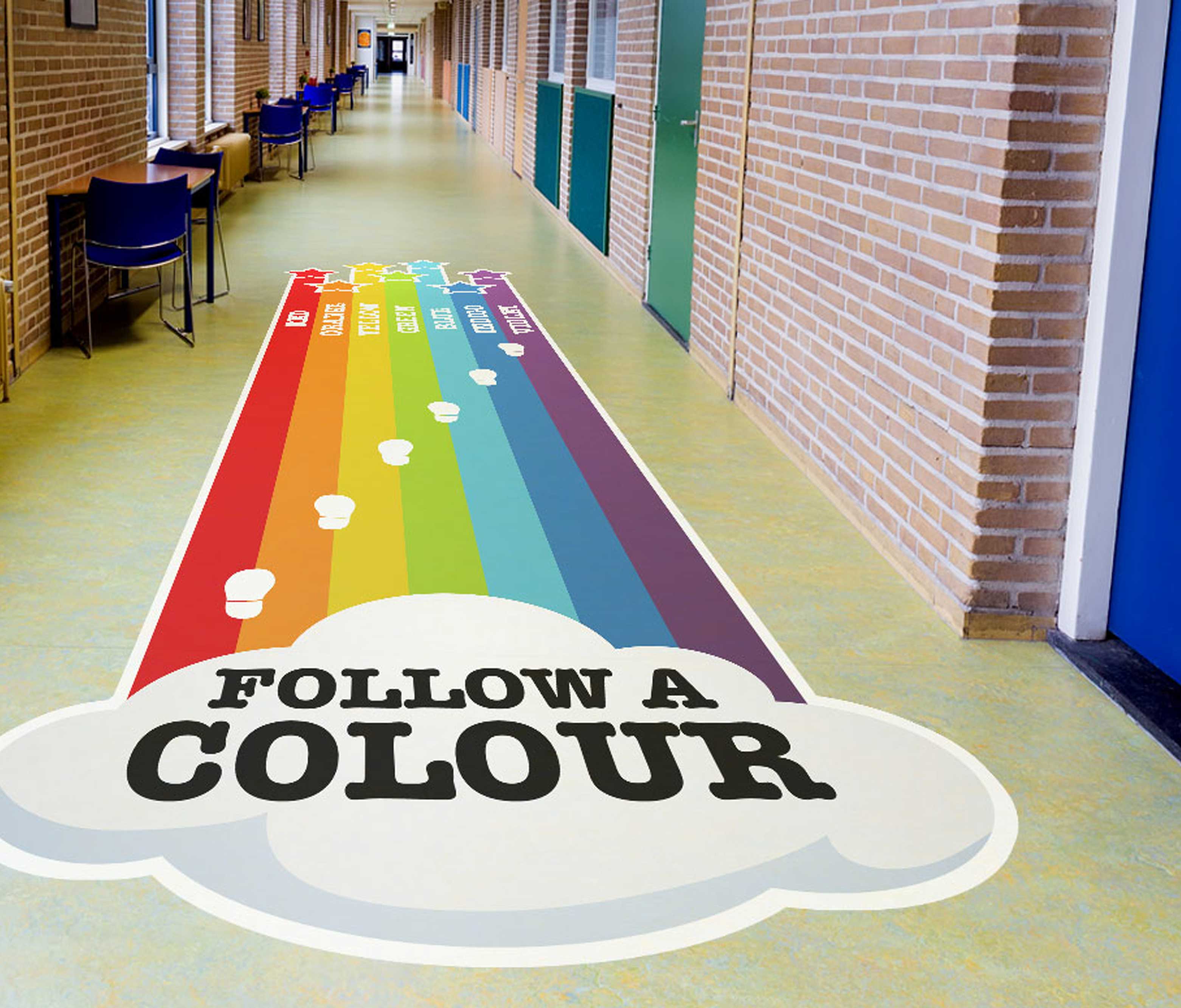 Bright rainbow floor vinyl with 'FOLLOW A COLOUR' text applied in an interior corridor as a directional wayfinding graphic, guiding people along colour-coded paths.