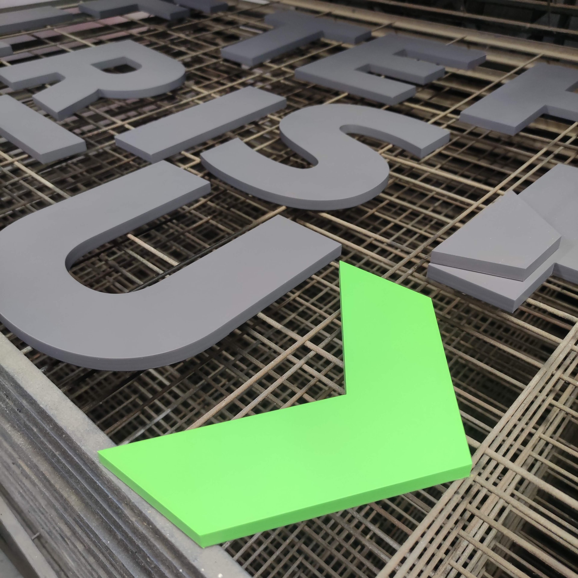 Painted cut letters and a bright green arrow panel laid out on a drying rack in a workshop spray/finishing area, ready for assembly or installation.