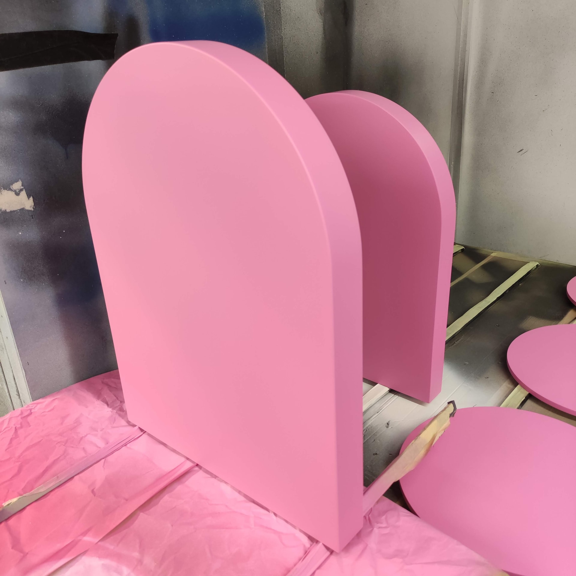 Pink arched display panels and round discs freshly spray-painted in a paint booth, likely part of a retail display or fixture production.