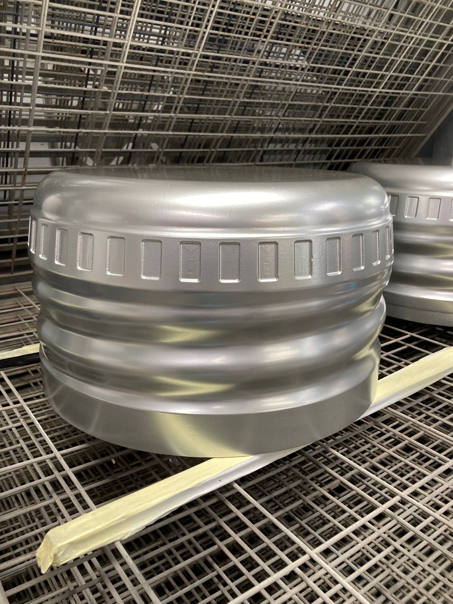 Silver spray-painted formed component drying on metal rack in a paint/finishing area, showing smooth metallic coating and masking.
