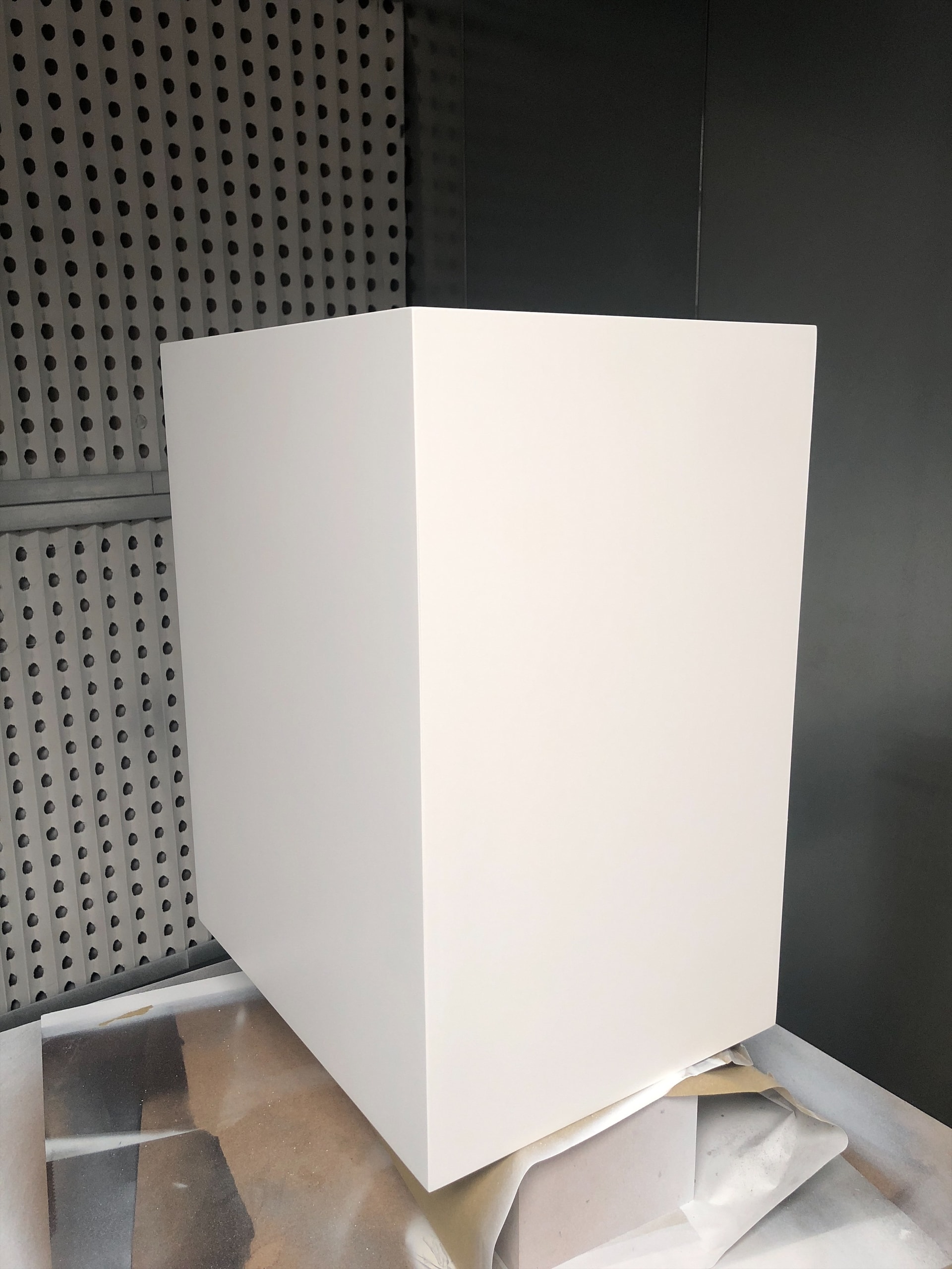 White painted rectangular enclosure photographed in a spray booth during the finishing stage, showing a smooth white finish and masking below.