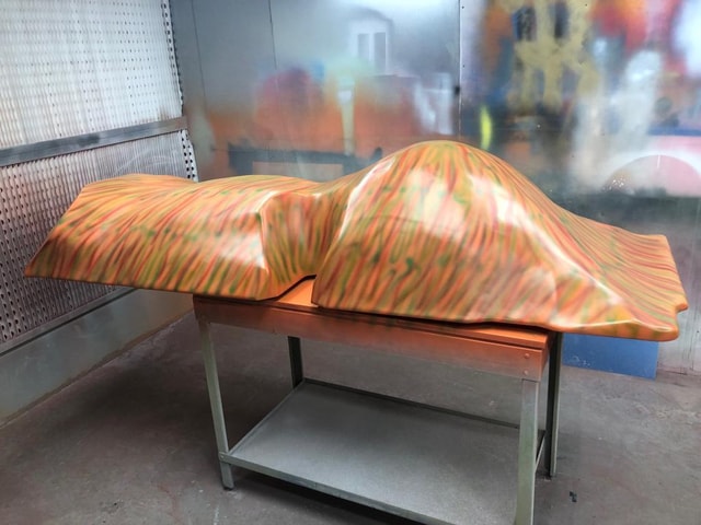 Vacuum-formed plastic shells with a multicolour sprayed finish sitting on a worktable inside a paint/spray booth, showing forming and finishing stages.